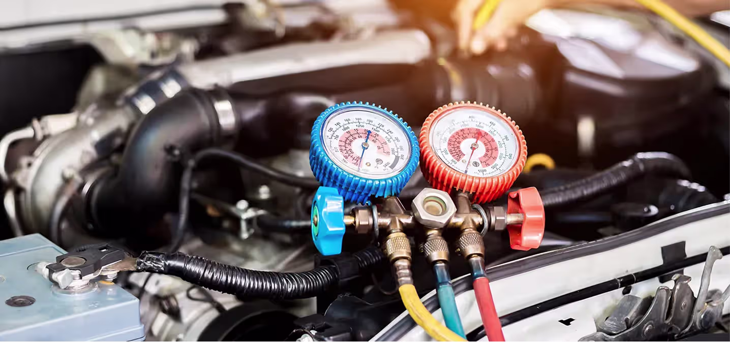 Auto air conditioning and heater repair in Naperville, IL at Clark's Car Care. A close-up of an automotive air conditioning manifold gauge set with blue and red dials attached to the engine bay of a car, indicating AC system pressure during maintenance.