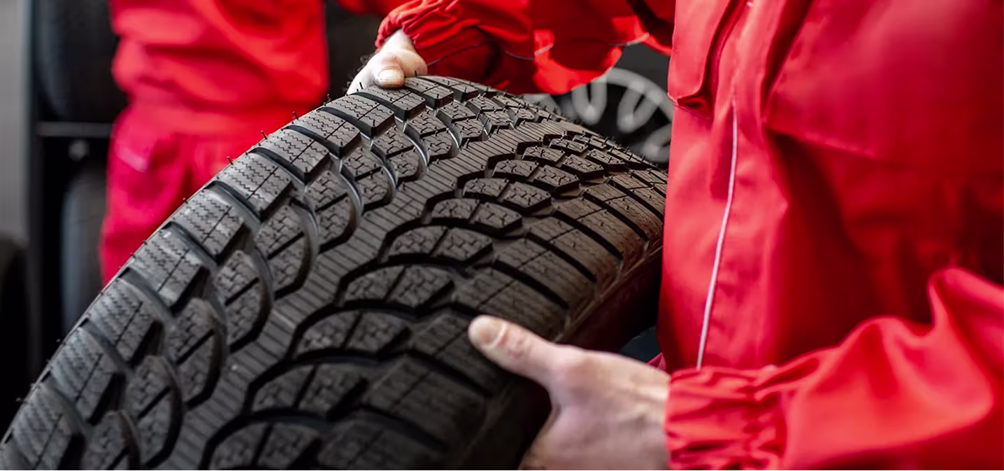 Tire services & sales in Naperville, IL at Clark's Car Care. A person wearing a red uniform holds a large car tire, showing the detailed tread pattern up close.